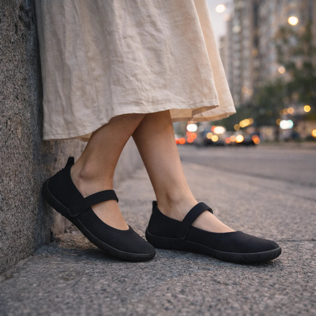 Detalle de calzado barefoot mujer negro apoyado en muro, destacando su diseño minimalista.