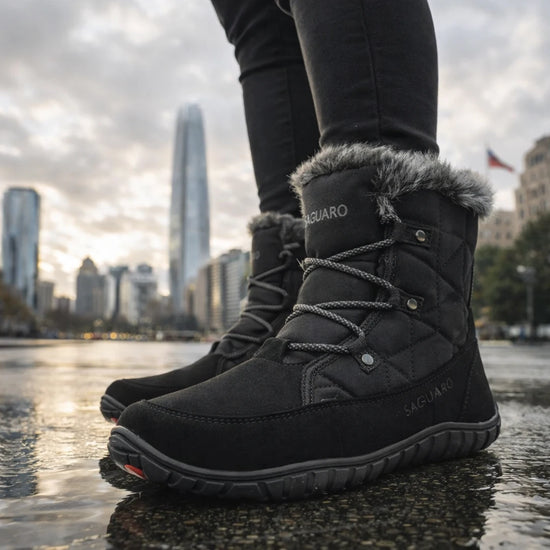 Mujer caminando sobre pavimento mojado con zapatillas anchas impermeables negras.