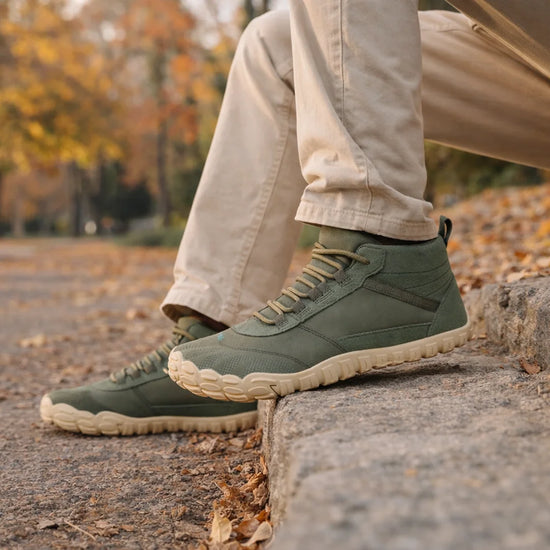 Persona sentada en escalones de piedra usando botas barefoot Saguaro Will I Lite verde, destacando su estilo casual y suela flexible para outdoor.