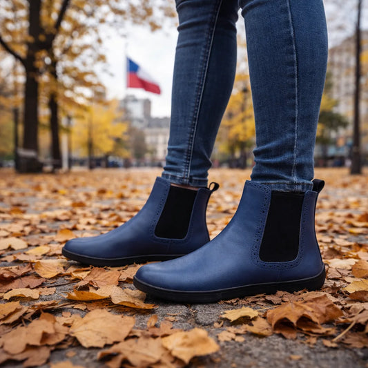 Hombre usando botines barefoot azules en un entorno urbano con hojas secas y bandera de Chile al fondo.