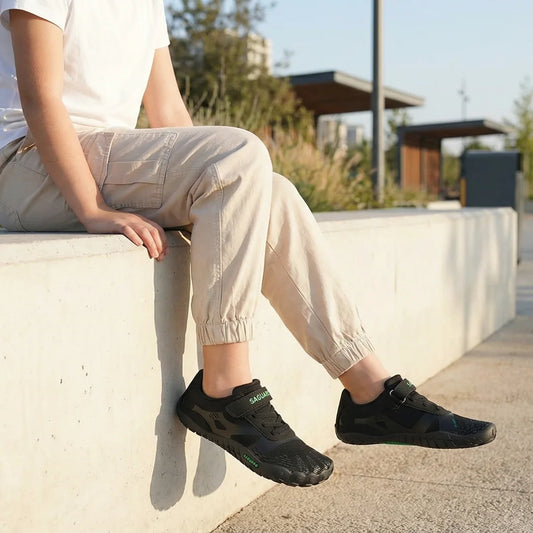 Niña sentada en un muro con zapatillas respetuosas Saguaro Vitality III 2.0 blancas, calzado ligero y transpirable para el tiempo libre.