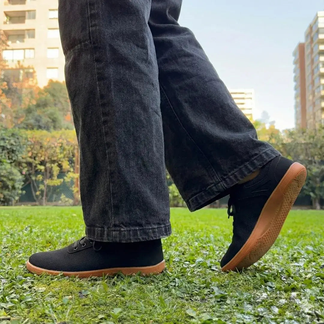 Primer plano de pies caminando en pasto con zapatillas barefoot negras.