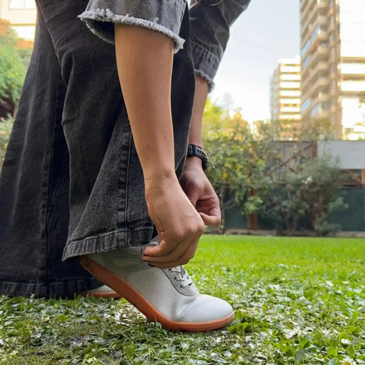 Mujer ajustando los cordones de su zapatilla minimalista ZZFaber gris.
