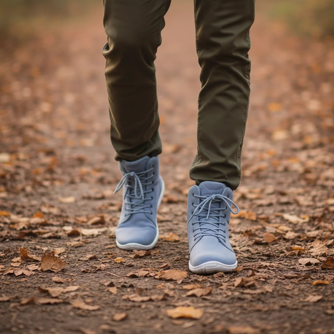 Hombre caminando sobre hojas secas con botas de invierno barefoot azules.