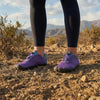 Mujer usando zapatillas barefoot púrpuras en sendero de tierra y naturaleza.