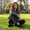 Mujer sentada en el césped usando zapatillas minimalistas ZZFaber negras.
