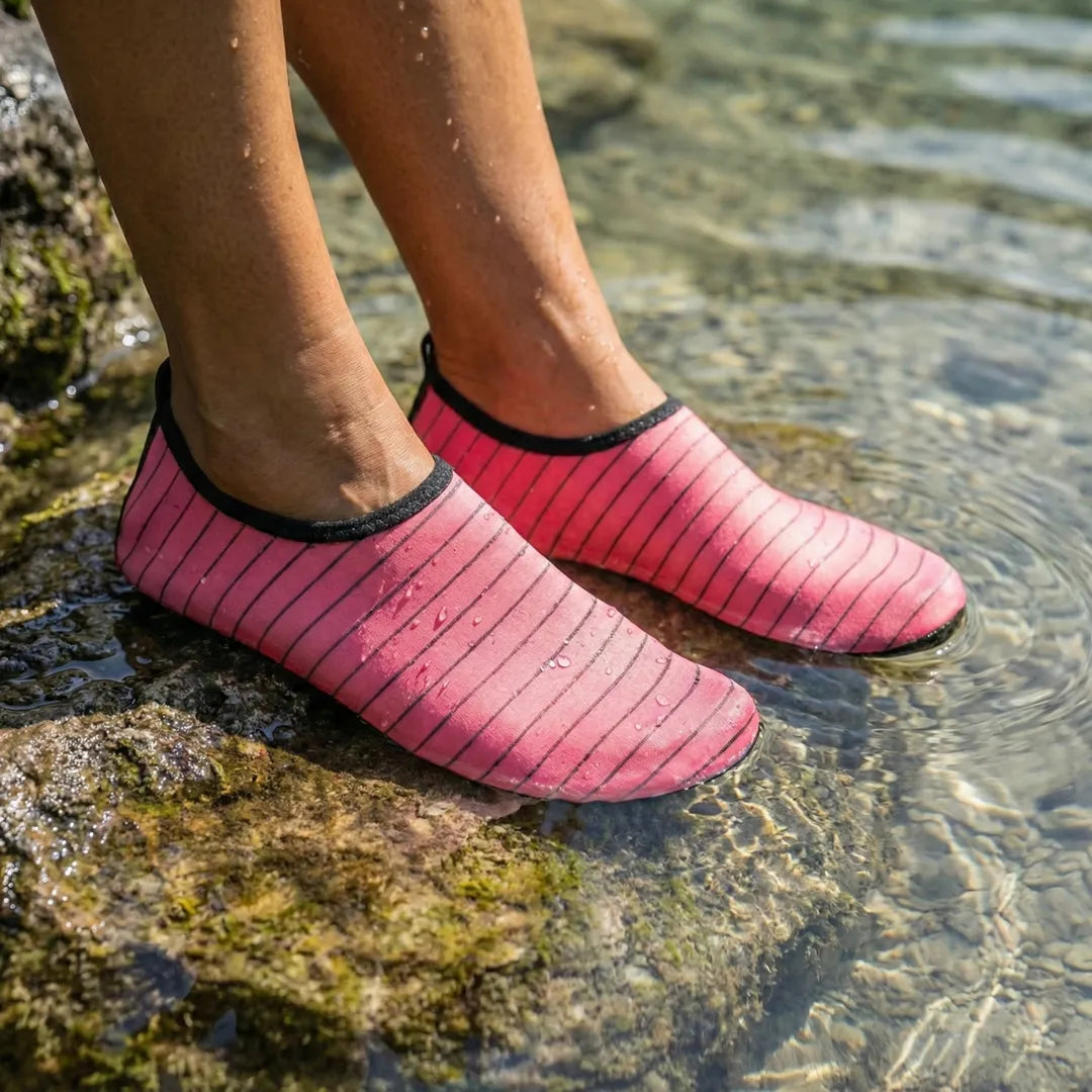 Primer plano de mujer sentada en rocas de río con zapatillas de agua rosas.