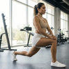 Mujer en gimnasio usando zapatillas barefoot blancas flexibles.