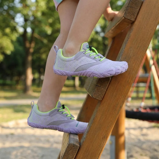 Niña jugando y escalando usando zapatillas barefoot Saguaro púrpura flexibles.