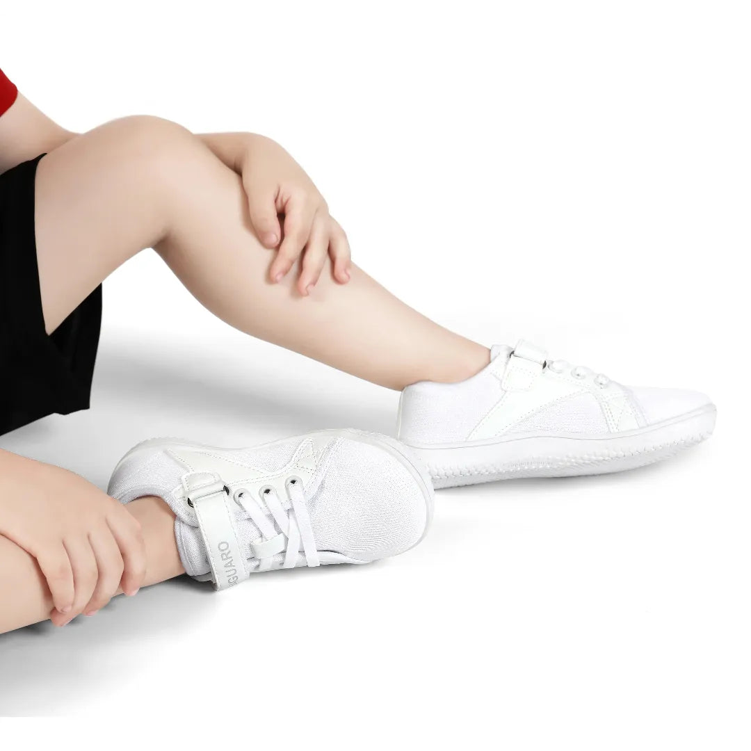 Foto niño usando zapatos barefoot Saguaro blancos, flexibilidad visible.