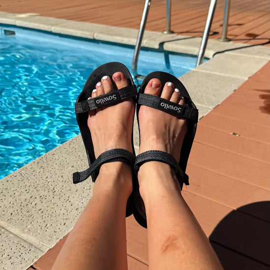 Persona usando sandalias Sowilo Raido negras al aire libre junto a una piscina.