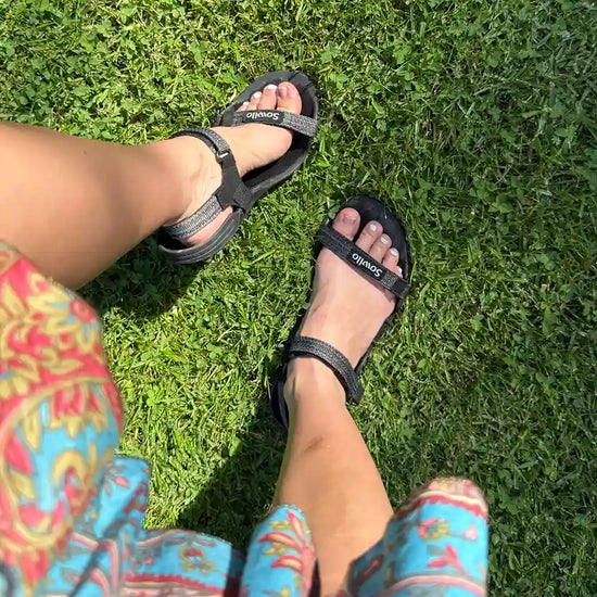 Persona usando sandalias Sowilo Raido negras al aire libre. 