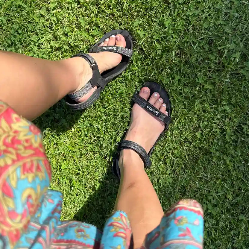 Persona usando sandalias Sowilo Raido negras al aire libre. 