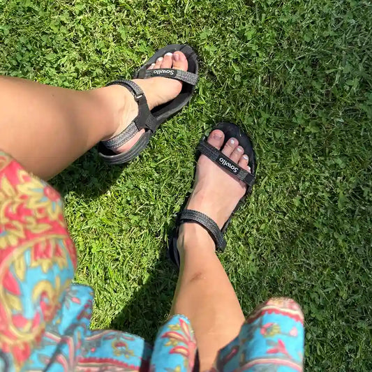 Persona usando sandalias Sowilo Raido negras al aire libre. 