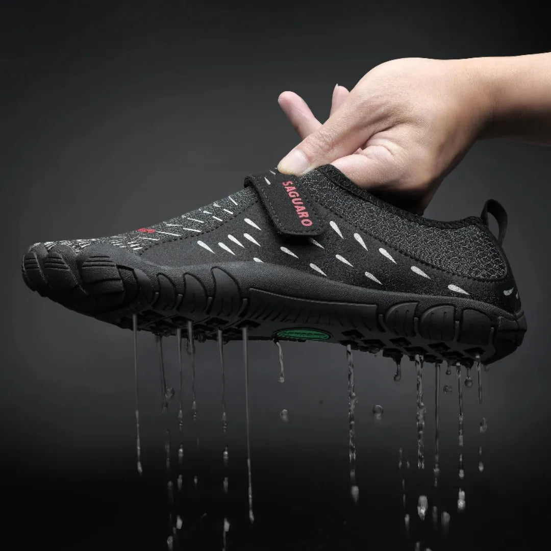 Mano sosteniendo zapatilla agua negra mostrando expulsión de agua por suela.