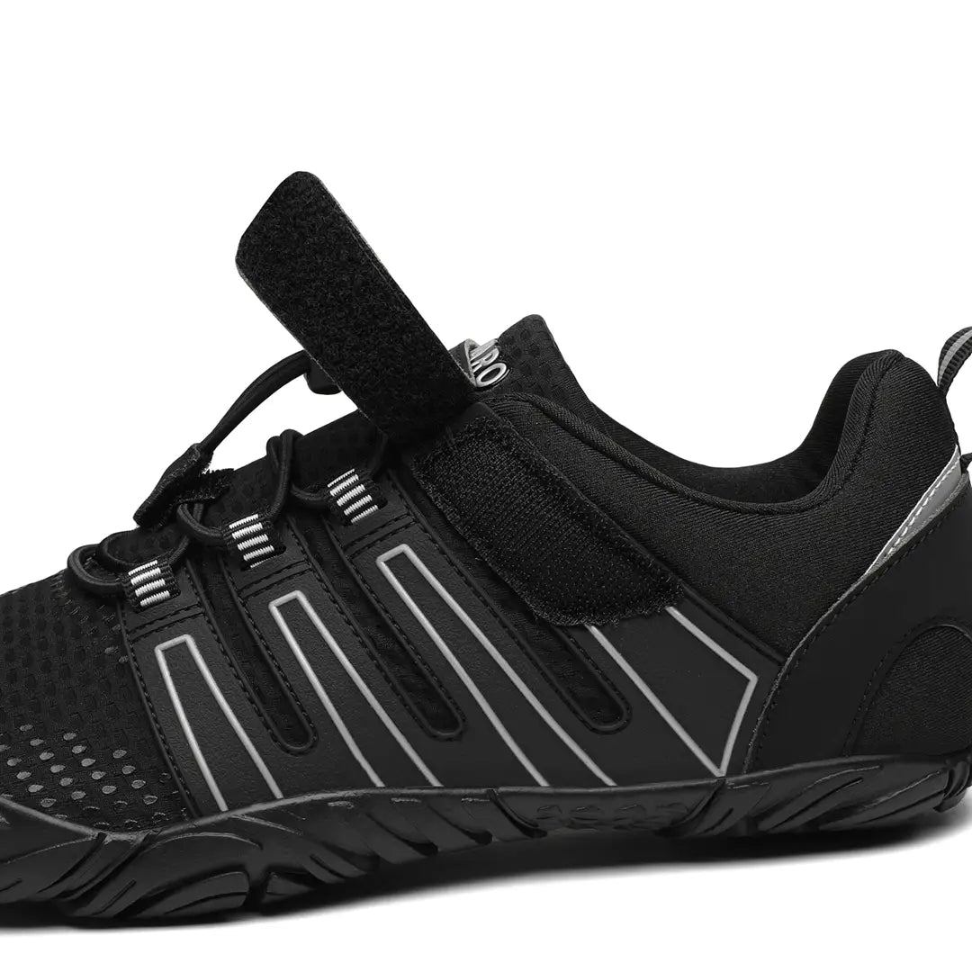 Detalle lateral de la zapatilla barefoot Saguaro Vigor II negra mostrando el cierre con velcro y materiales.