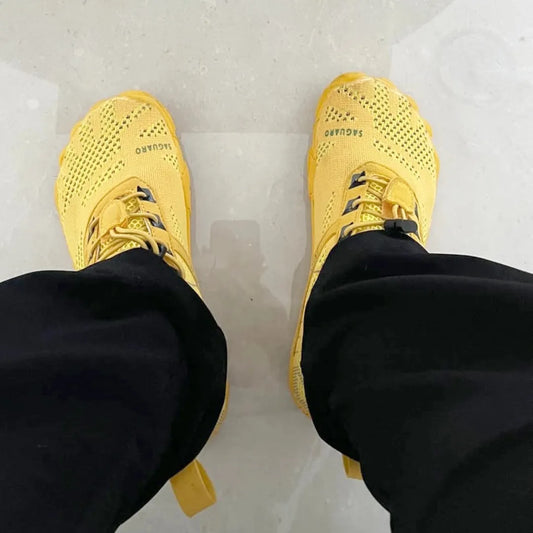 POV pies usando zapatillas Saguaro Free I amarillas, puntera ancha visible.