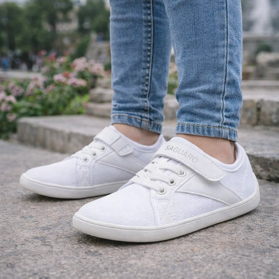 Niño usando zapatillas blancas barefoot de malla transpirable para caminar natural.