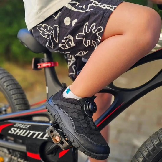 Niño usando zapatillas deportivas escolares en bicicleta, demostrando versatilidad.