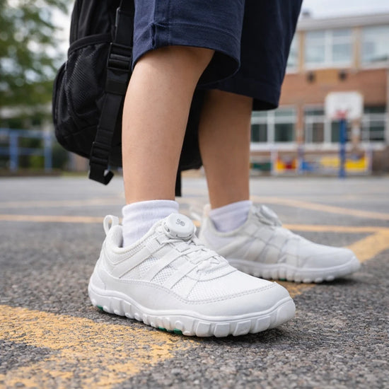 Niño caminando con zapato deportivo blanco barefoot en el patio del colegio.