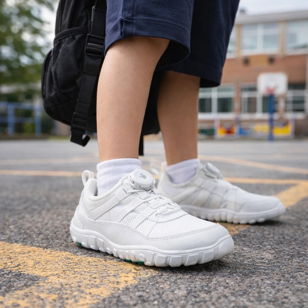 Niño caminando con zapato deportivo blanco barefoot en el patio del colegio.
