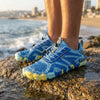 Persona de pie sobre rocas en la playa usando zapatillas azules Saguaro Active II.